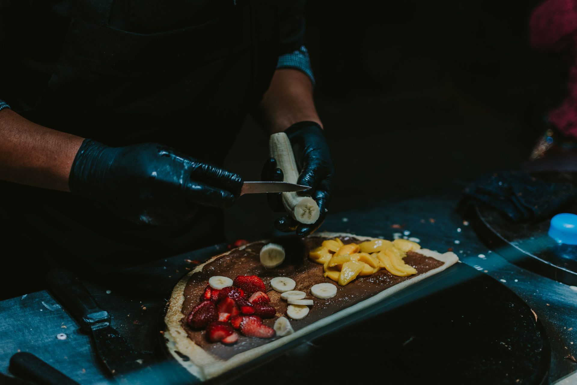 Ein Koch schneidet Obst für einen köstlichen Crêpe mit Erdbeeren, Bananen und Mango auf – ein perfekter Street-Food-Genuss.