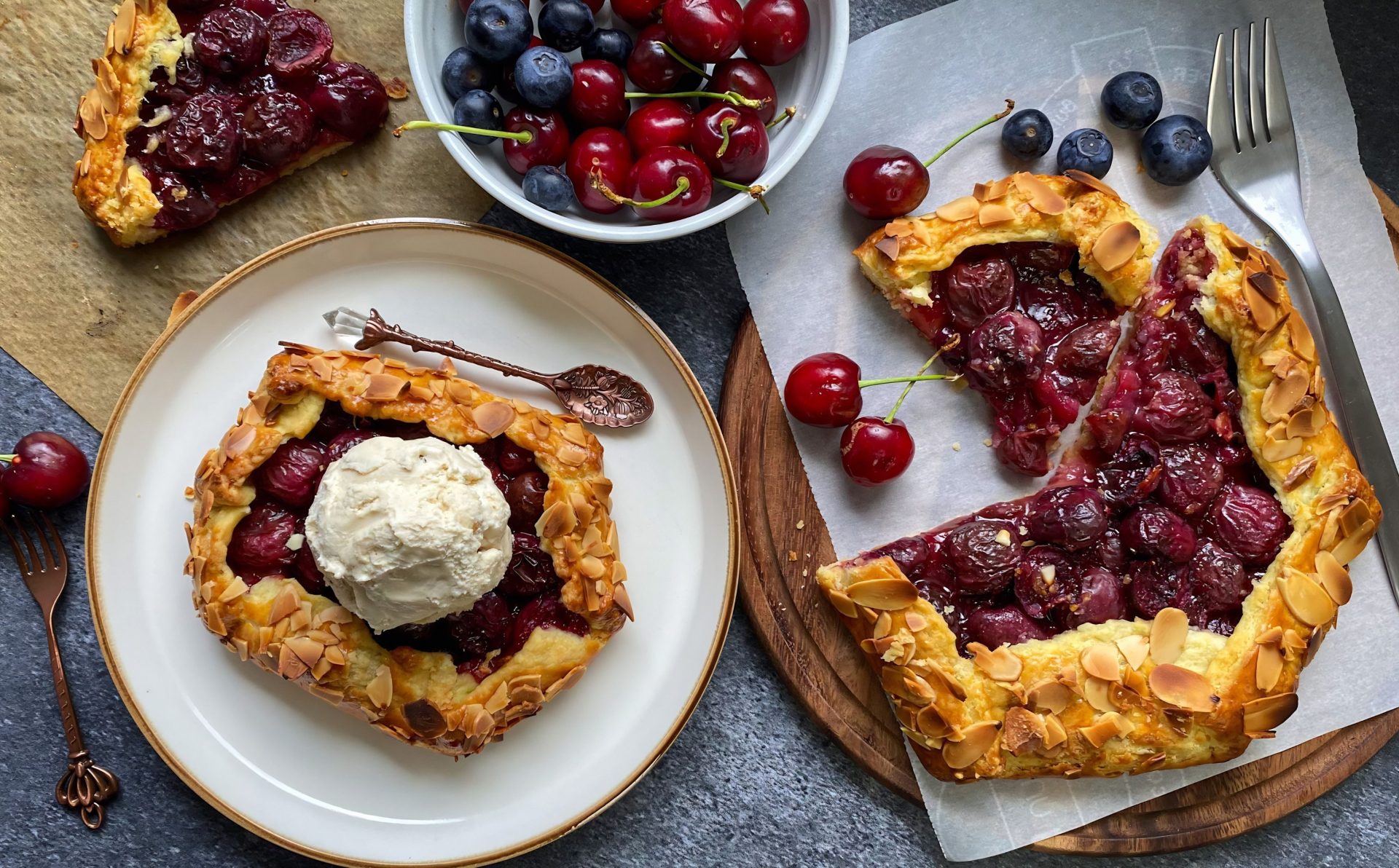 Rustikale Kirsch-Galette mit Eiscreme, umgeben von frischen Beeren auf einer strukturierten Oberfläche.
