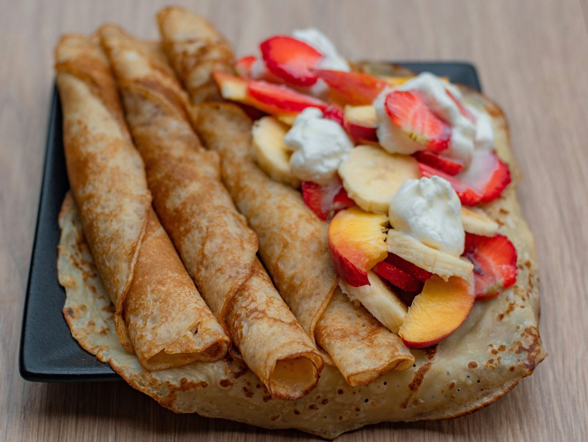 ein schwarzer Teller mit Crêpes, die mit Obst belegt sind